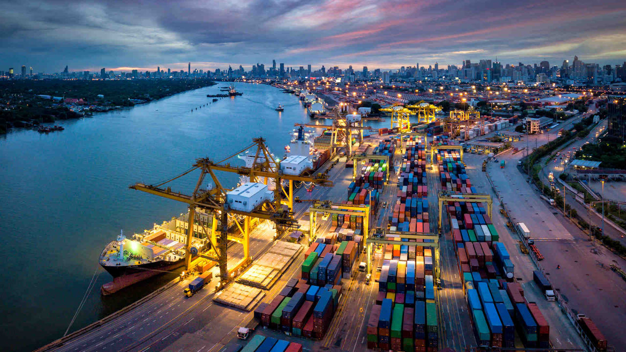 Aerial view of international port with Crane loading containers in import export business logistics with cityscape of Bangkok city Thailand at night