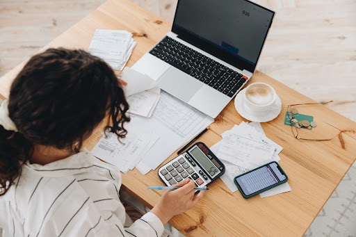 Top view of a woman working at home in the kitchen with financial papers, counting on a calculator, paying bills, planning a budget to save some money. Independent accounting, remote accountant.