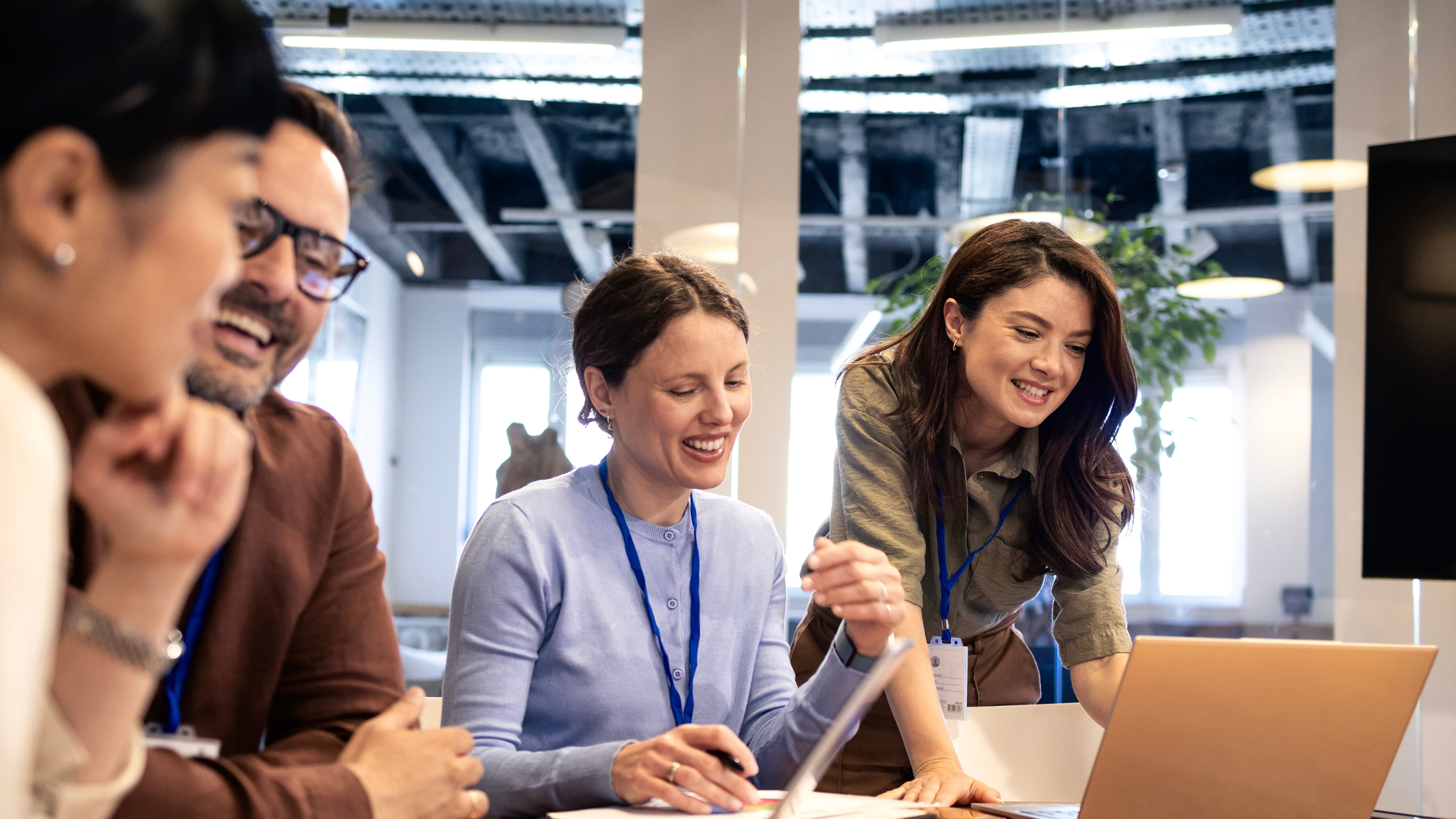 A group of four smiling professionals looking together at a laptop screen in a modern office.