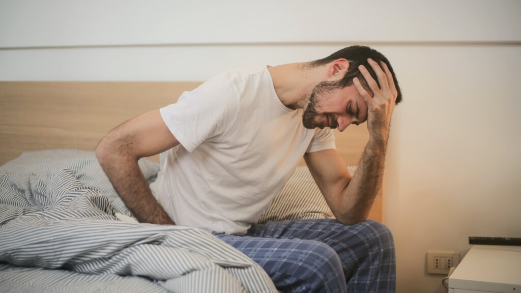 men with pain expression sits on a bed