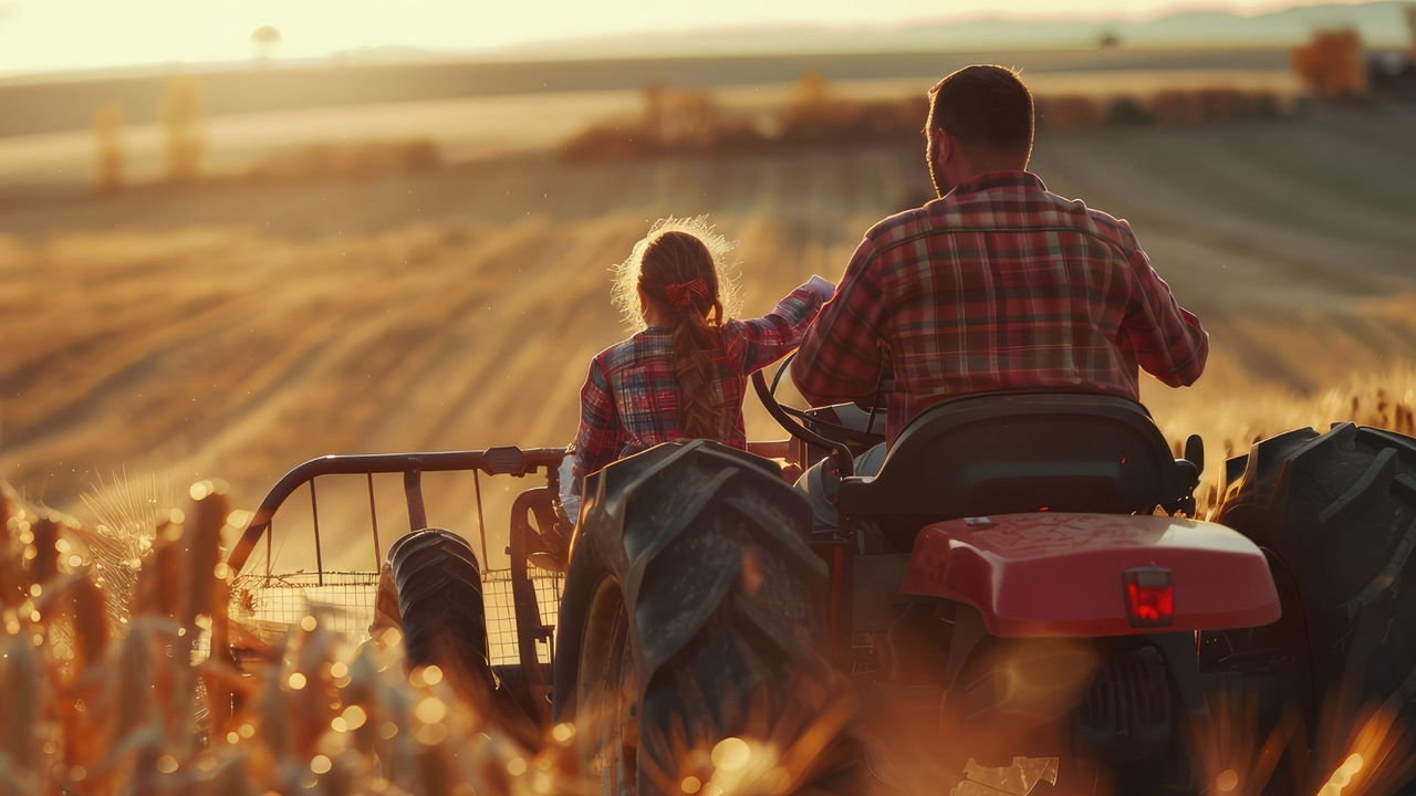 A farmer and his daughter drive a tractor at sunset.
