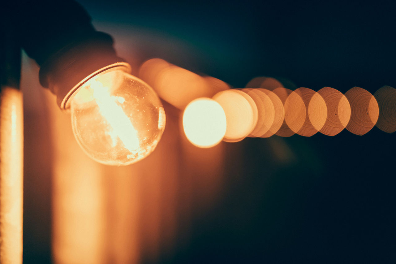 A close-up of a glowing round light bulb with a blurred string of warm-toned lights in the background