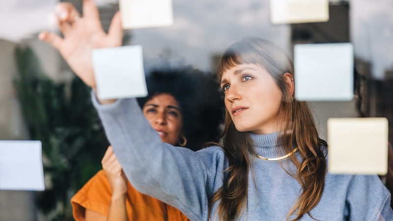 Two people working as a team organizing sticky notes on a glass wall.