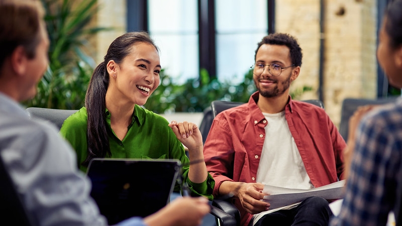 A group of people sitting in a circle, engaged in a relaxed conversation in an office setting.
