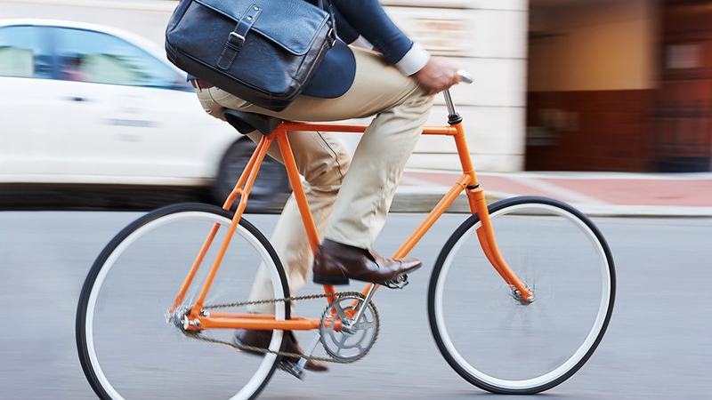 A person riding an orange bicycle along a city street.