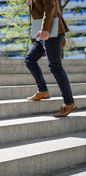 Hombre joven sube escaleras con un portátil en  la mano