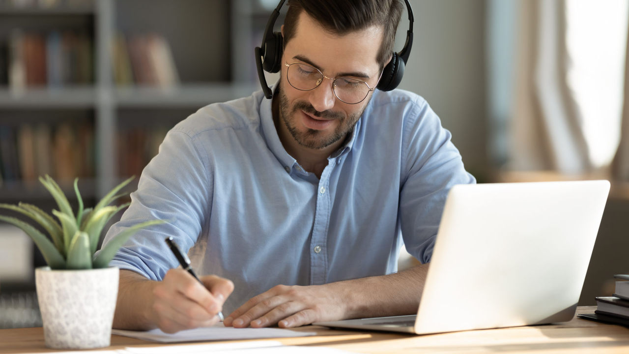 hombre con auriculares, bolígrafo y portátil