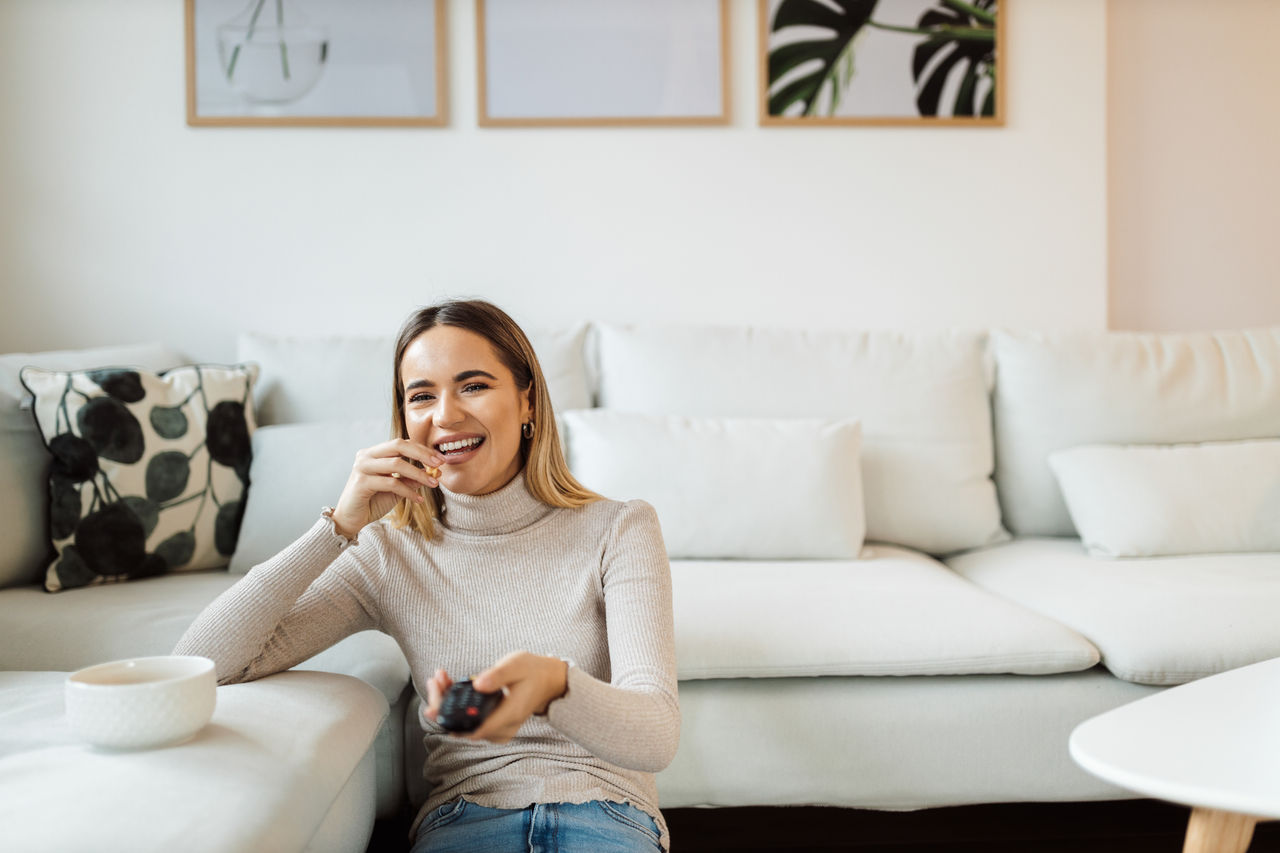 Girl holding a remote control, while eating some snacks and watching movie.