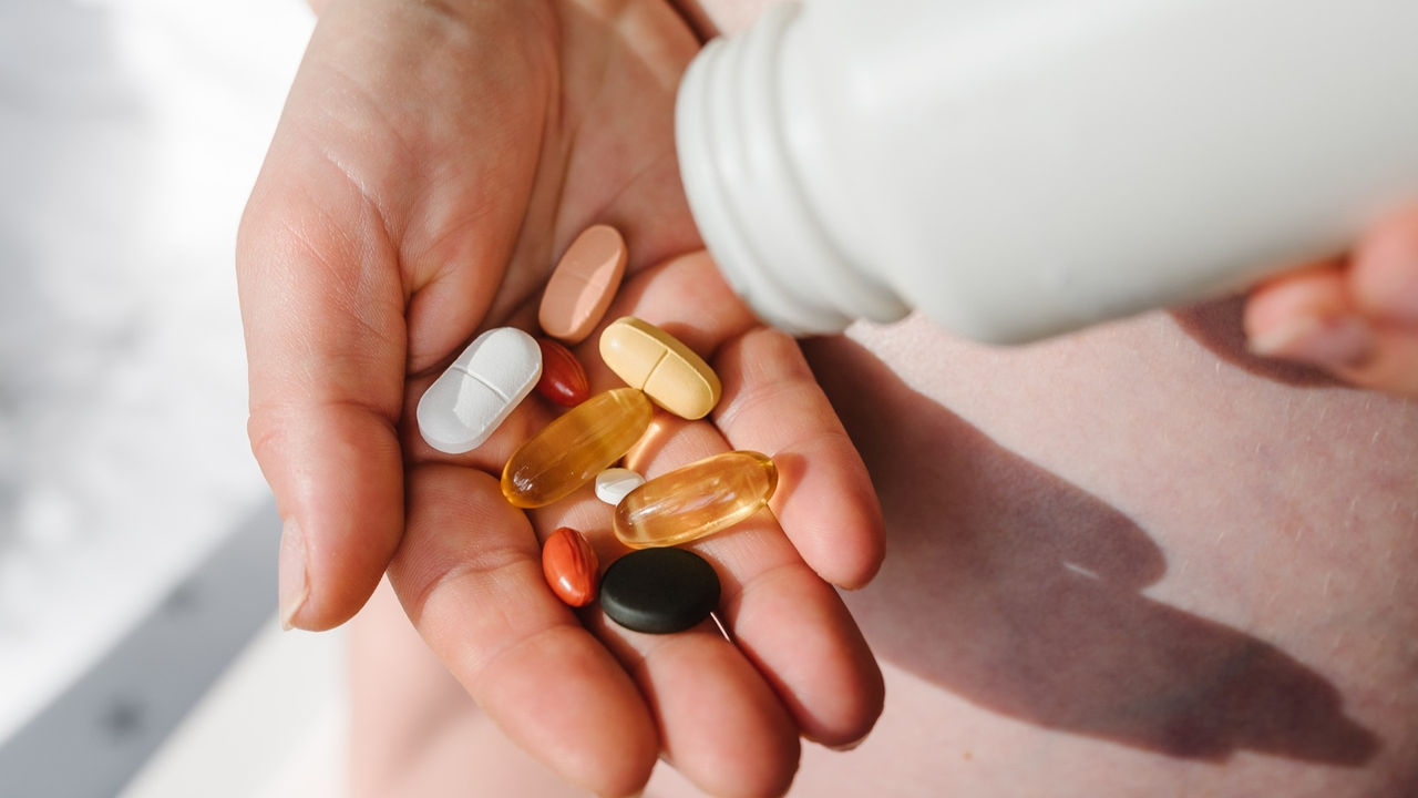 Closeup photo of supplements with a white bottle. Pregnant woman take omega 3, multivitamins, vitamins B, C, D, collagen tablets, probiotics, iron capsule. Girl hold vitamins daily. Top view.